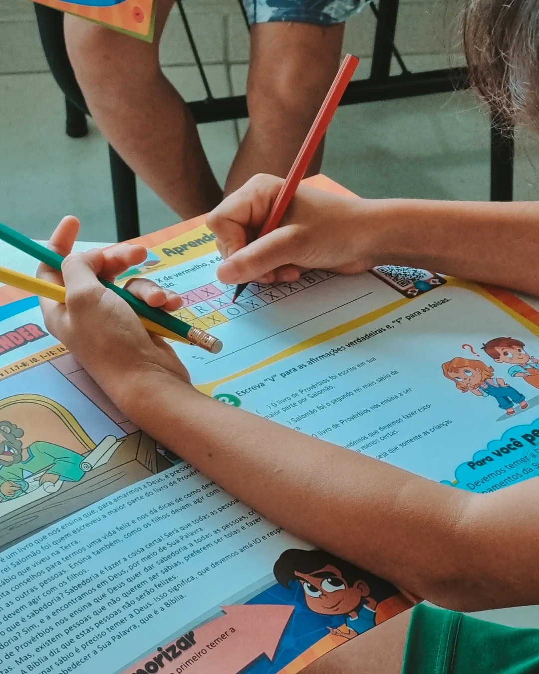 Mãos de uma criança respondendo, com lápis de cor, uma atividade bíblica sobre o livro de Provérbios