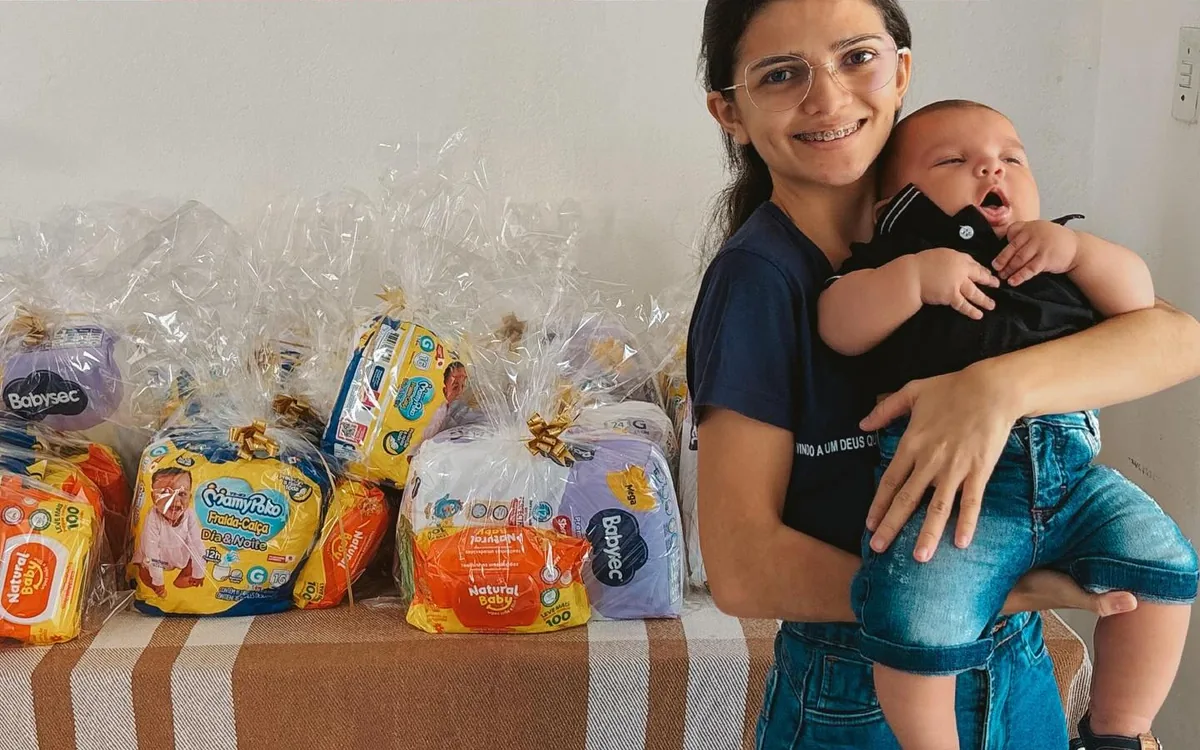 Voluntária segura um bebê ao lado de kits com fraldas preparados para as famílias