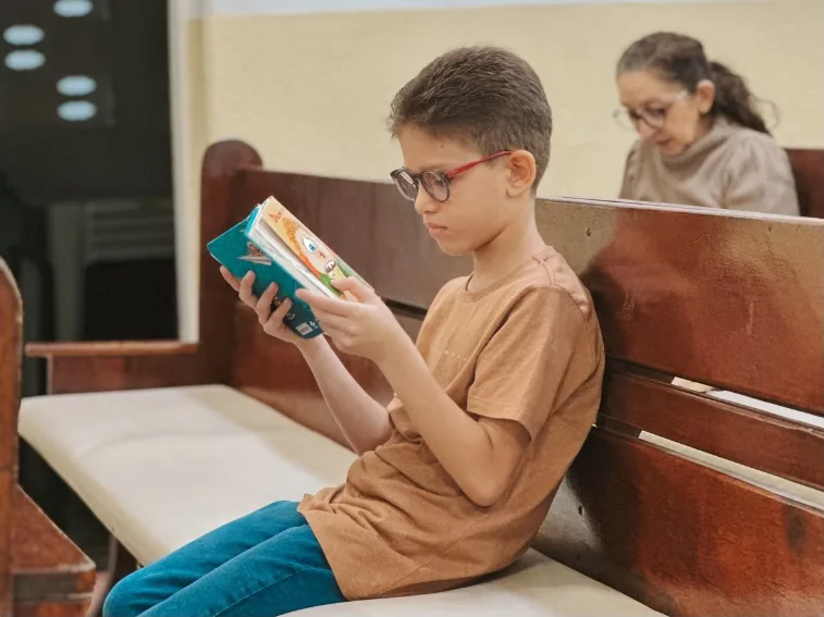 Menino sentado no banco da igreja, lendo um livro com atenção