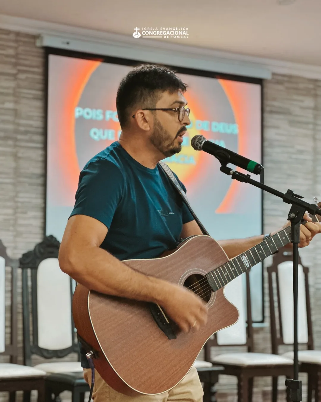 Músico ao violão conduzindo os cânticos, com a letra projetada ao fundo