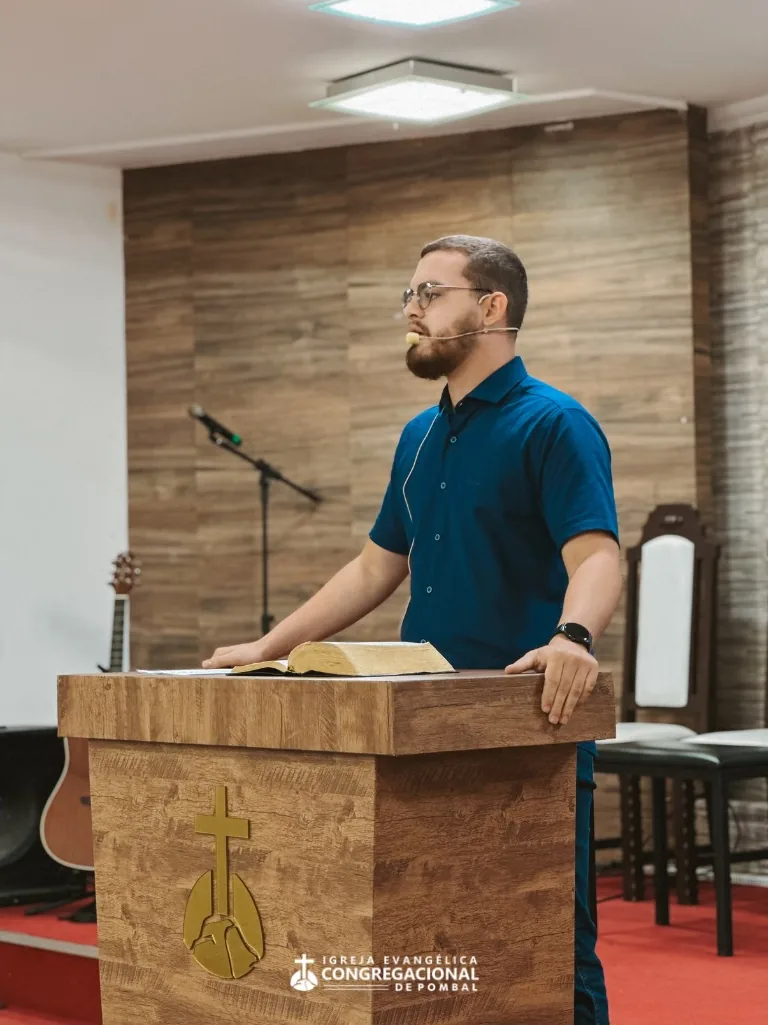 Pregador ao púlpito com a Bíblia aberta; à frente do púlpito, o símbolo da cruz da igreja
